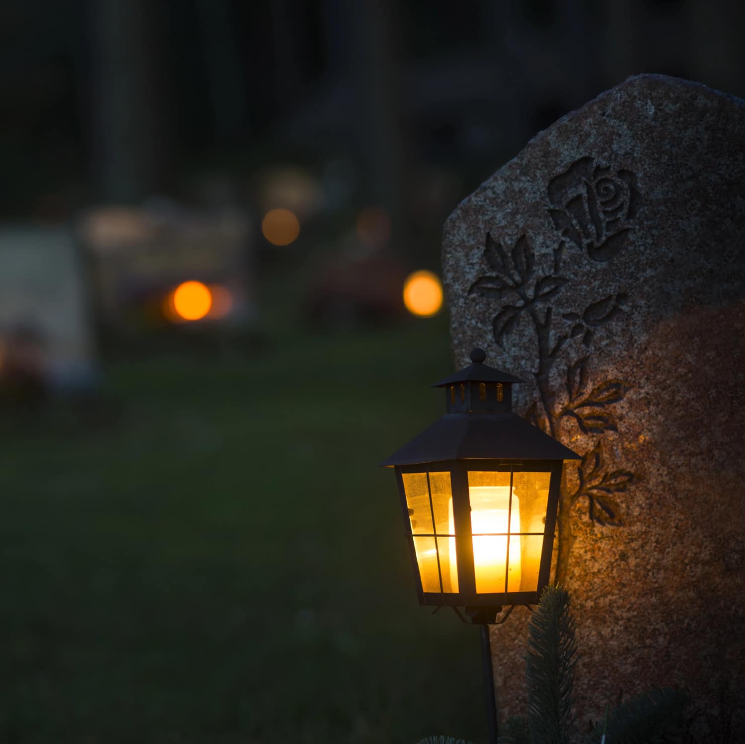 Kynttilan valo loistaa hautalyhdyssa hautakiven vieressa.