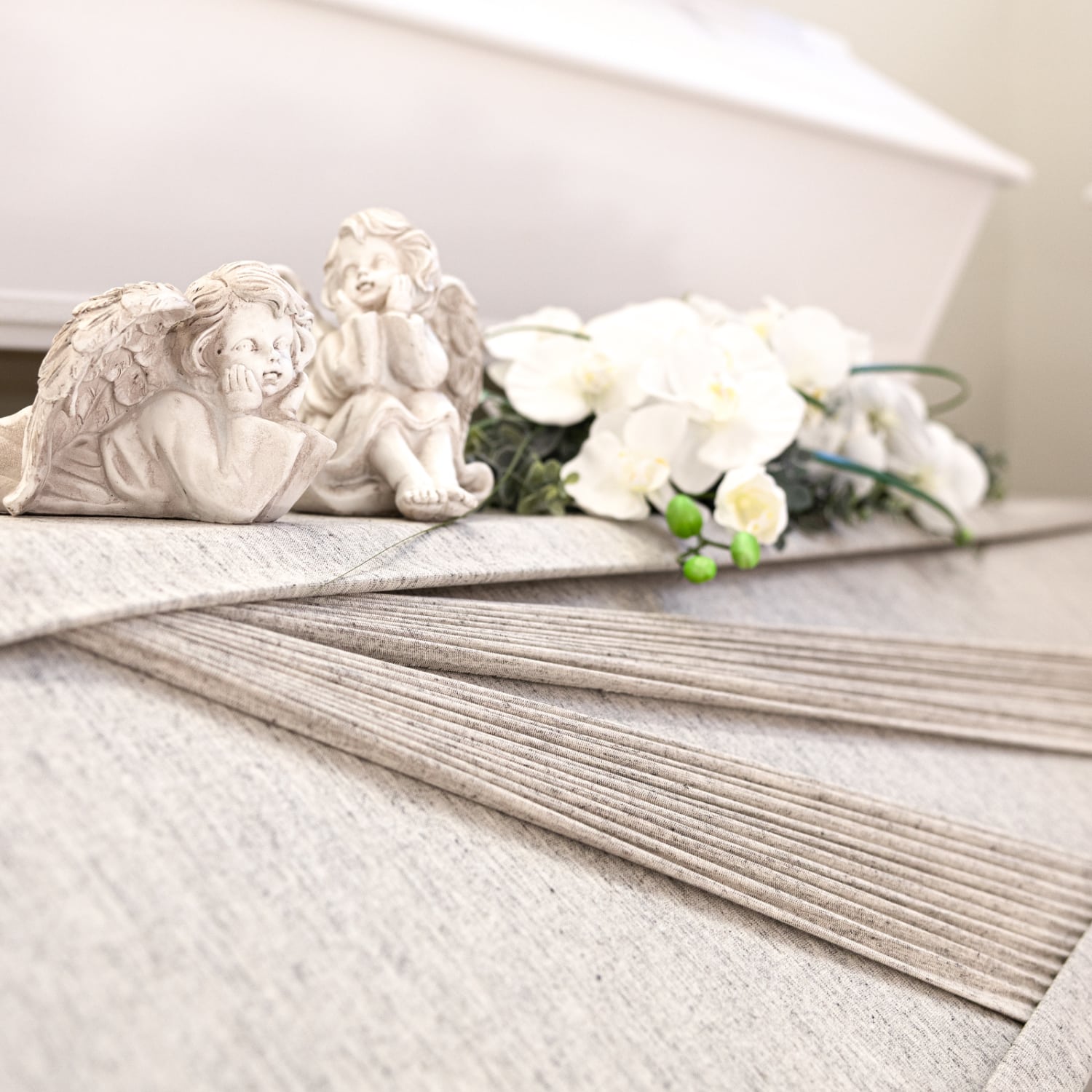 Heinimaen-Hautaustoimisto-hautauspalvelut-Rauma-Eura-Eurajoki-Laitila-Pyhamaa-Pyharanta-arkut Vaalean hauta-arkun paalla enkelikoristeet ja valkoiset kukat.