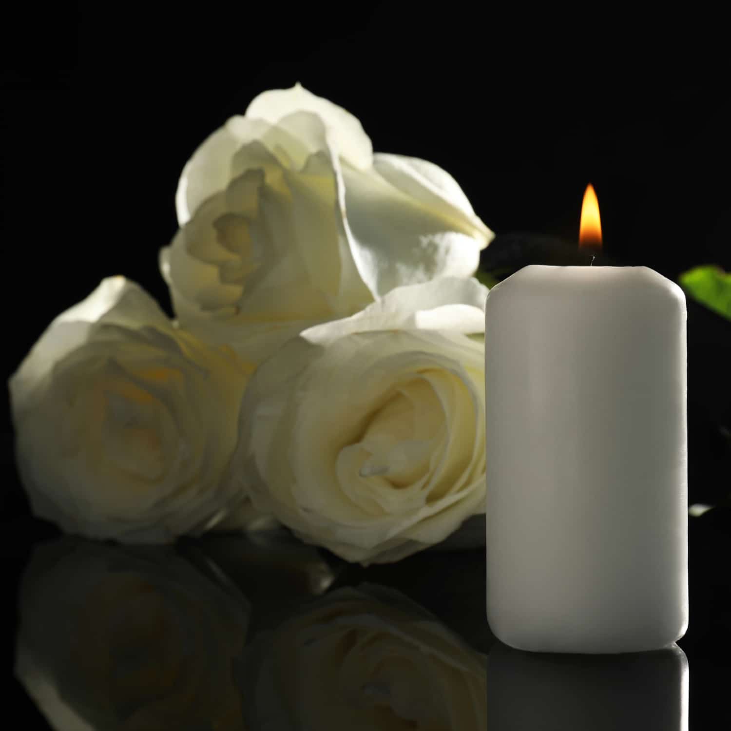Valkoinen kynttila palaa valkoisten ruusujen vieressa.